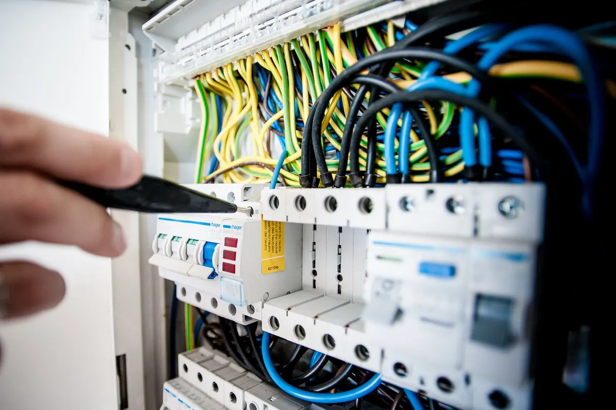 Electrician's hand on a circuit breaker panel with color-coded wiring
